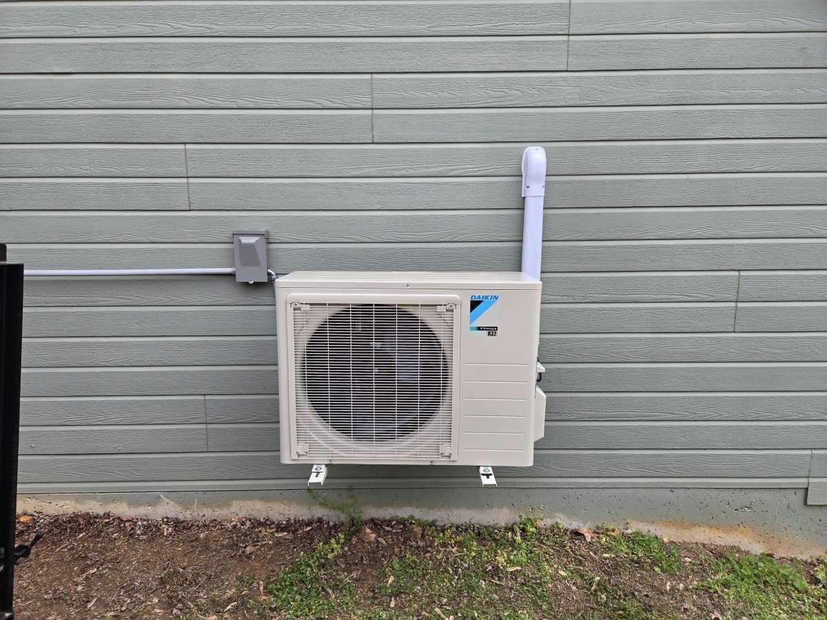 Outdoor wall-mounted air conditioner unit on a light green house exterior.
