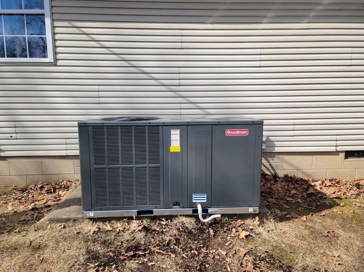 Outdoor HVAC unit beside a house with beige siding and bare ground around it