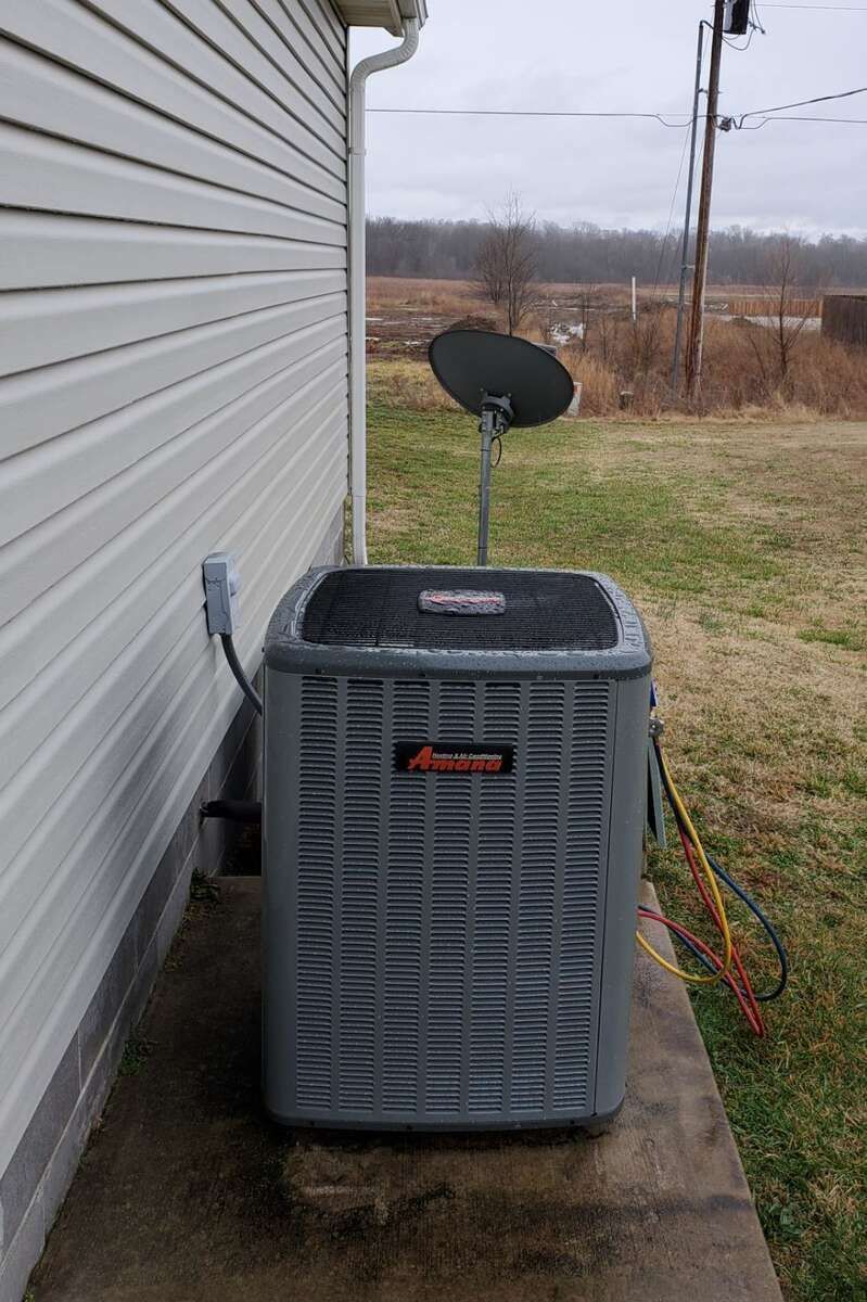 Outdoor HVAC unit beside a house with a small satellite dish and wet concrete patio.