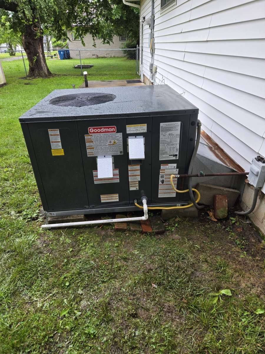 Outdoor air conditioner unit beside a white house on a grassy side yard