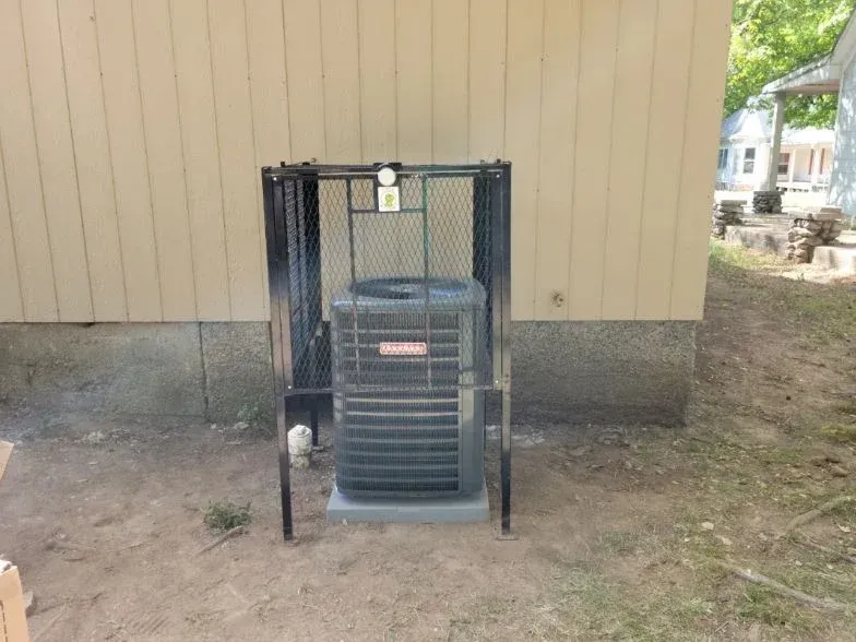 Outdoor air conditioner unit behind a black metal cage beside a tan building.