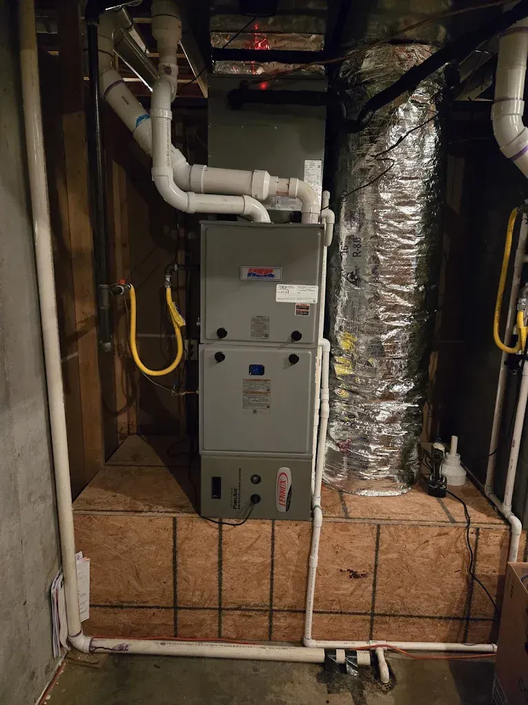 Gray HVAC furnace in a basement utility area with exposed pipes and insulated ductwork.