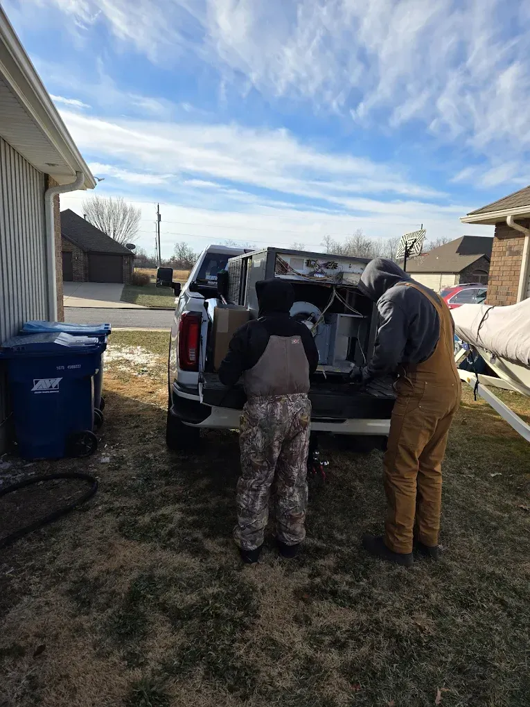 Two people loading items from the back of a white pickup truck in a suburban yard
