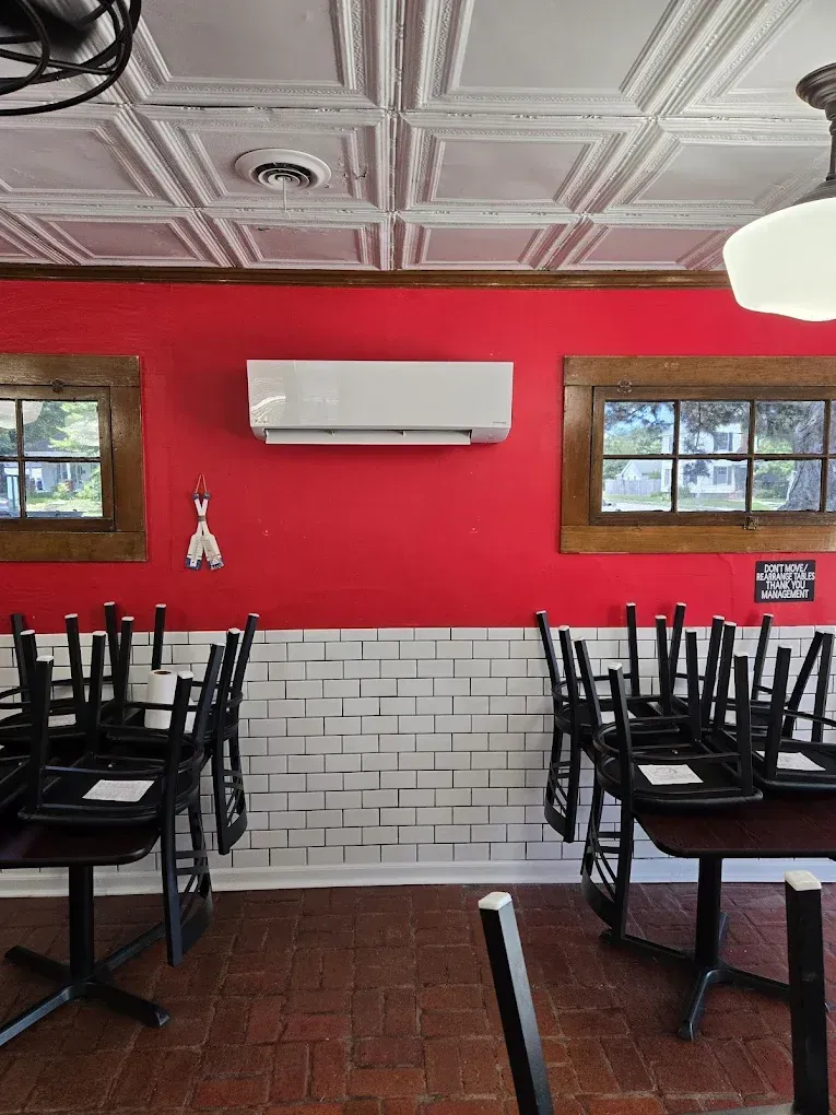 Empty restaurant interior with red wall, white ceiling, wall AC, and stacked black chairs on tables