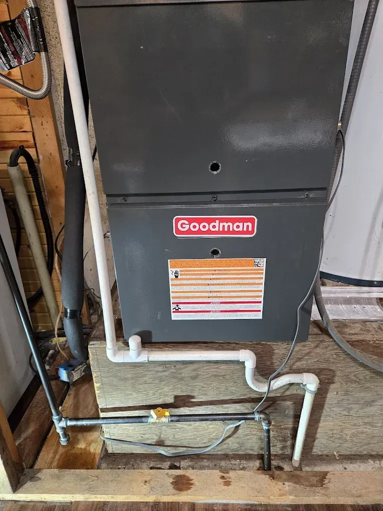 Goodman furnace with white PVC pipes and exposed utility lines in a basement area