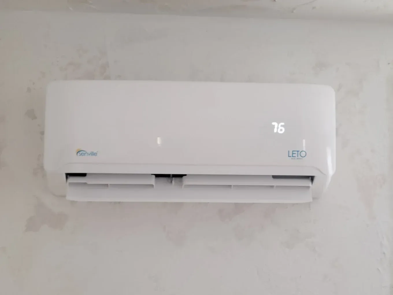 White wall-mounted air conditioner with a digital display showing 76 on a plain wall.