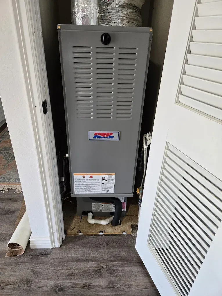 Gray furnace/air handler in a hallway closet with open louvered door and exposed vent ducting.