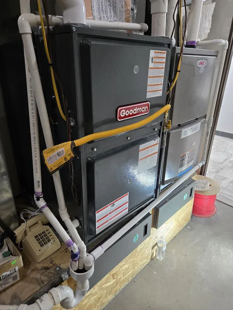 Two gray furnaces in a basement mechanical room, with pipes and yellow caution tape across the front.