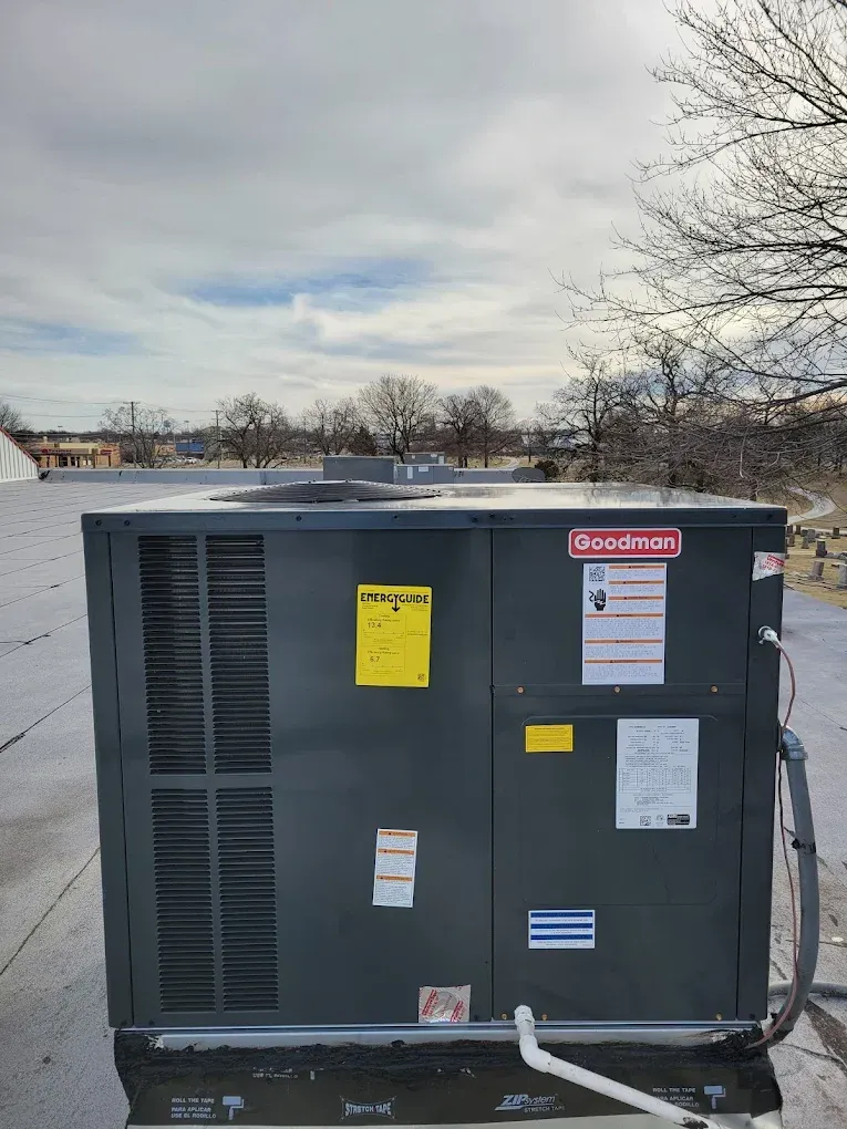 Gray rooftop HVAC unit with warning labels on a flat roof under a cloudy sky
