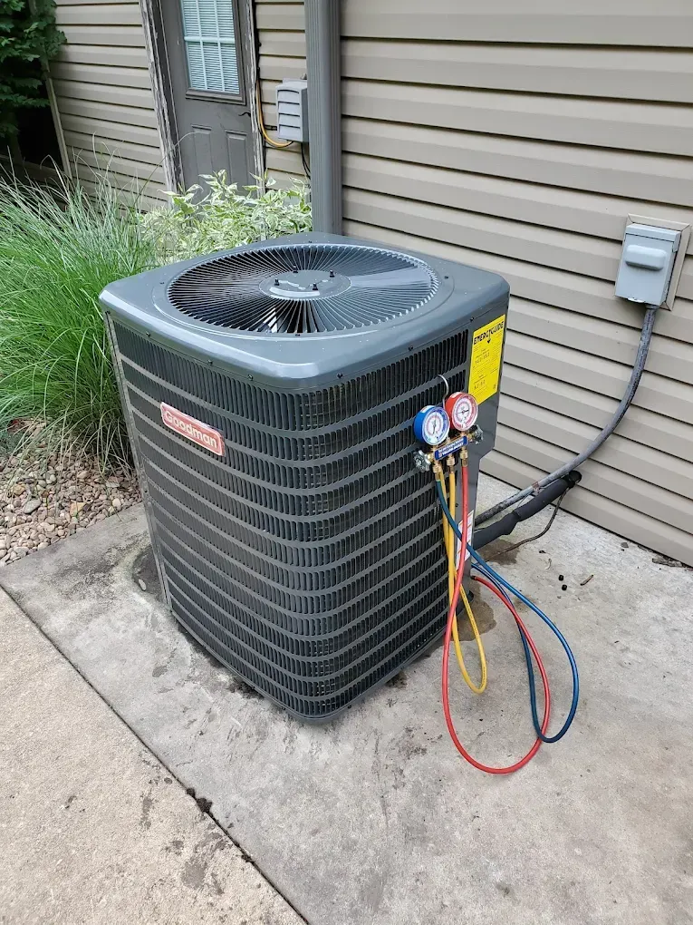 Outdoor air conditioner unit with attached refrigerant gauges and hoses beside a house wall