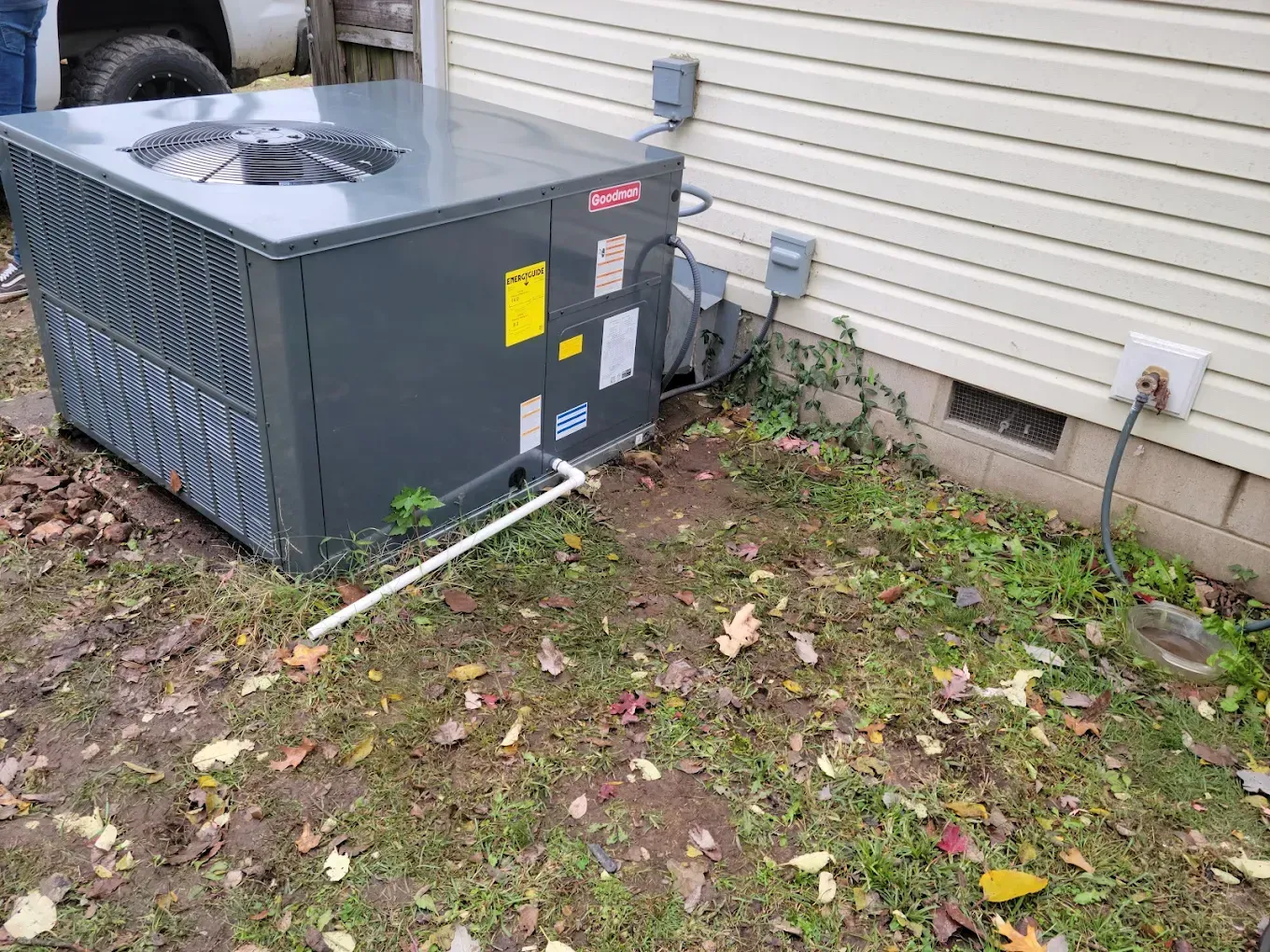 Outdoor HVAC unit beside a house, with hoses and electrical connections near a beige siding wall.