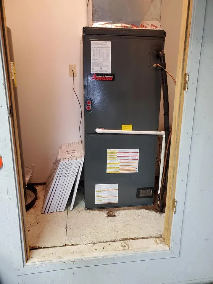 Gray HVAC furnace in a narrow utility closet with labels, beside stacked vent filters.
