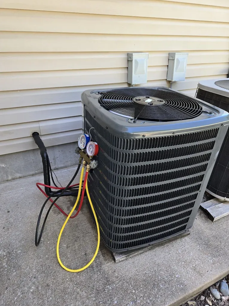 Outdoor HVAC unit with service gauges and hoses attached beside a house siding