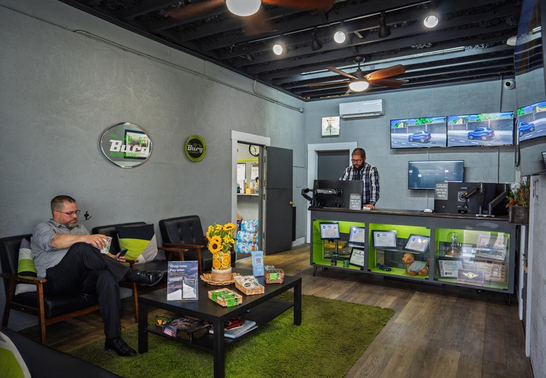 Modern office lobby with a person seated on a couch, a reception desk, and display monitors.