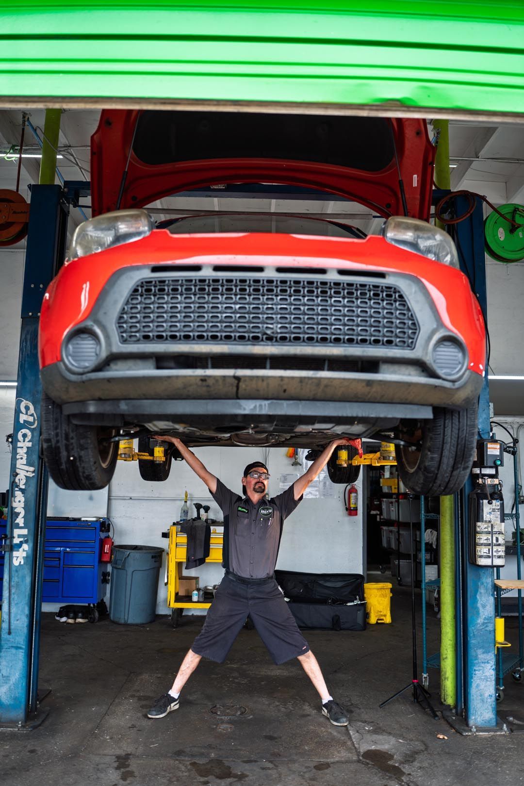 Mechanic lifting a red car on a lift in an auto shop, arms raised beneath the vehicle