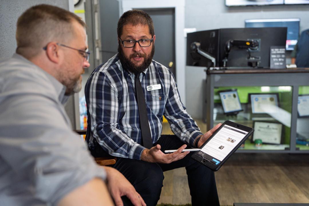 Two men talking in an office, one holding a tablet with a digital form.