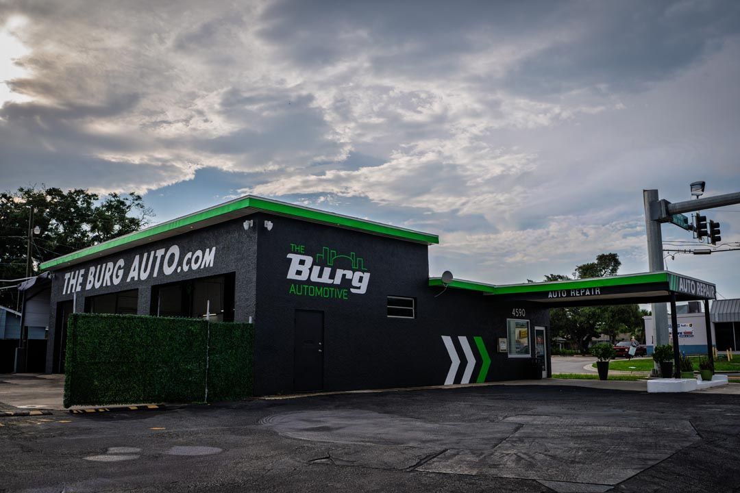Exterior of a green auto shop with a cloudy sky and empty parking lot at dusk
