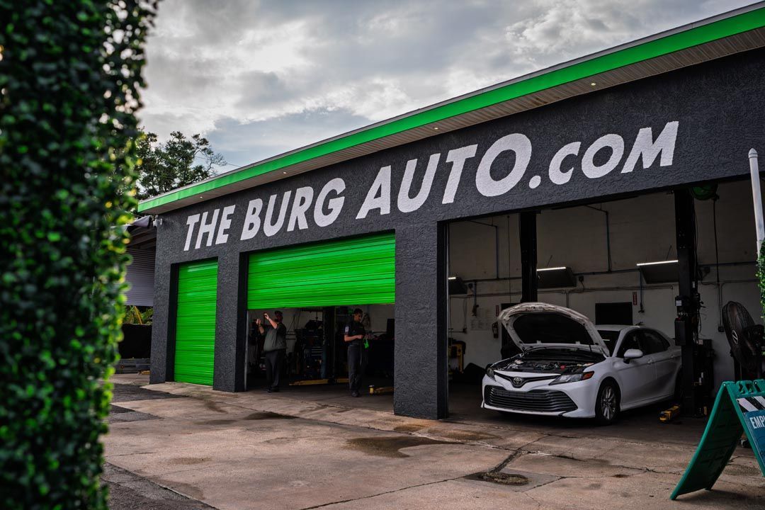 The Burg Auto.com storefront with green garage doors and a silver car parked outside