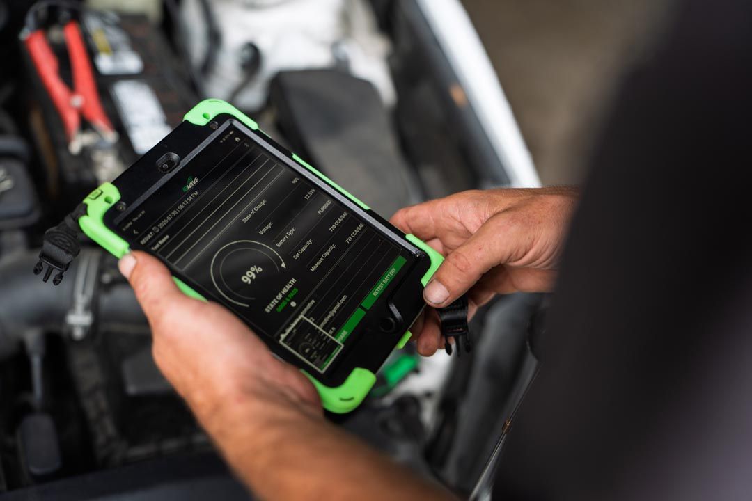 Person holding a green-cased tablet showing vehicle diagnostics in a car engine bay