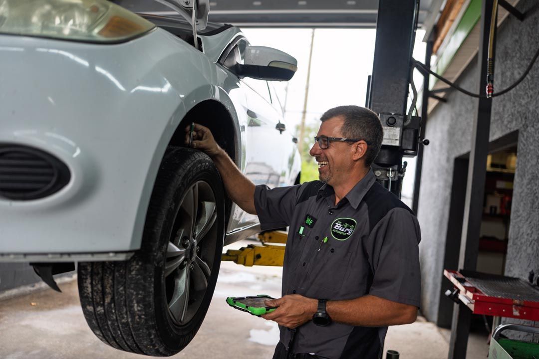 Mechanic inspecting a white car’s front wheel in an auto shop