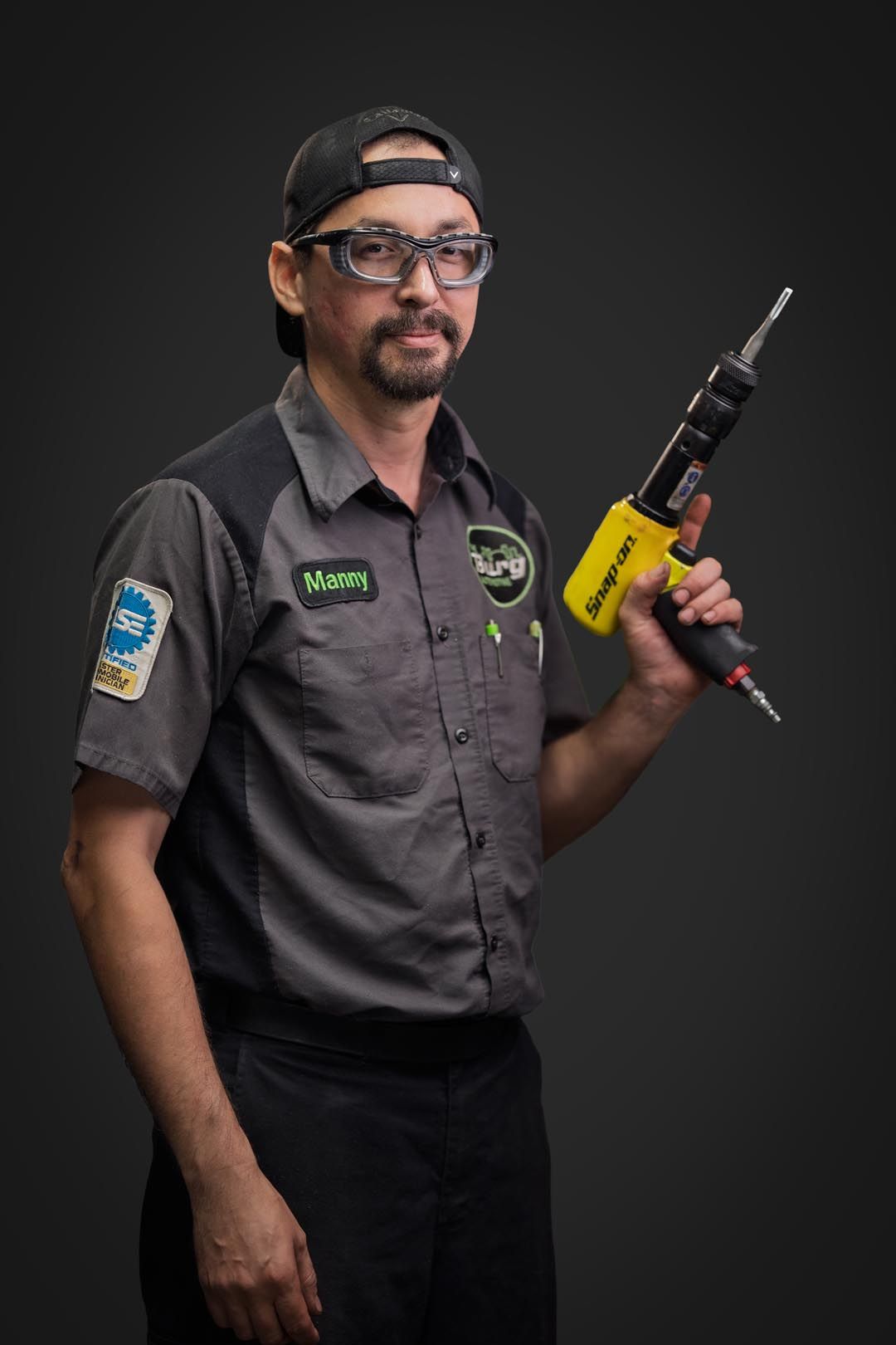 Mechanic in gray uniform holding a yellow cordless drill against a dark background