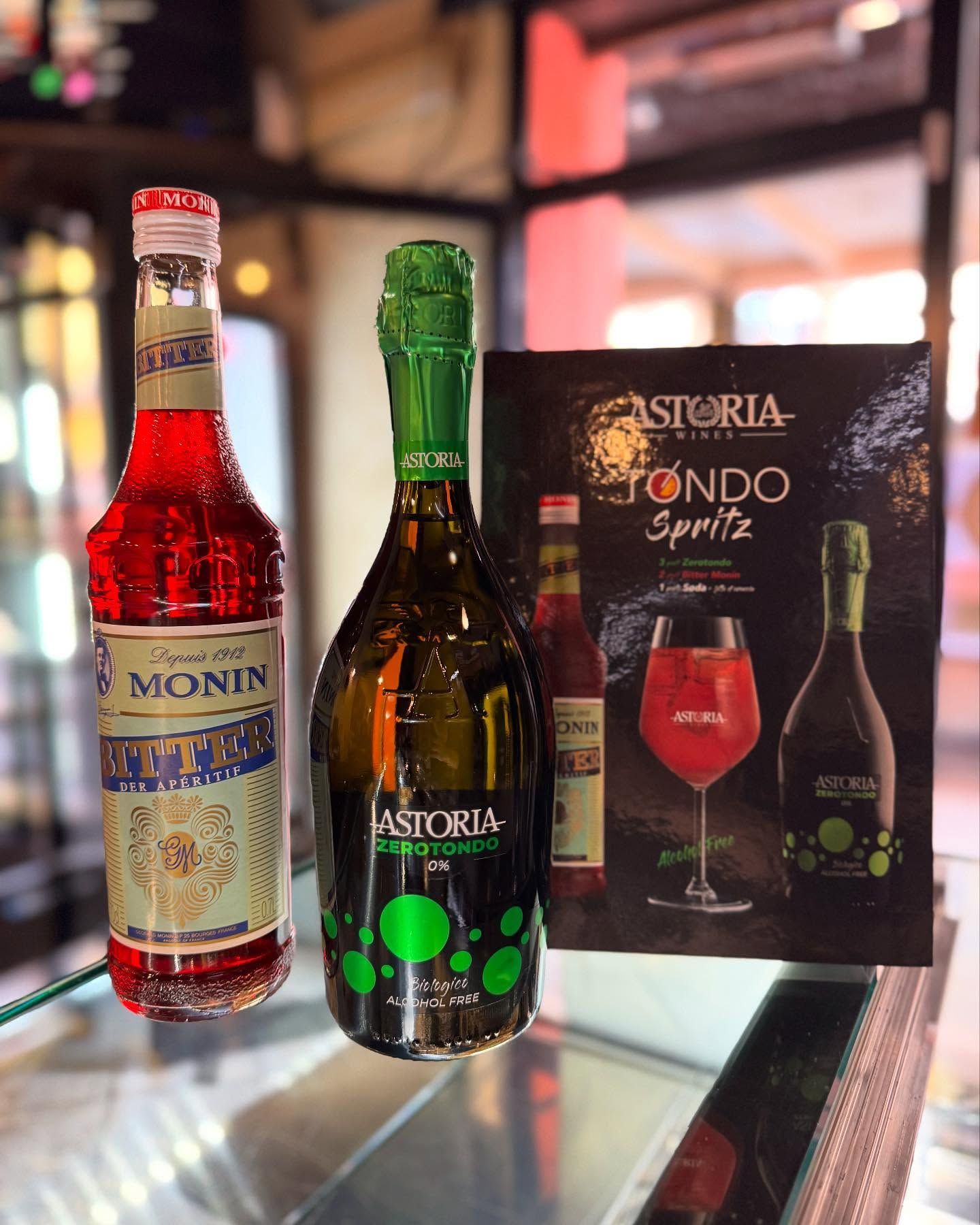 Bottiglie di sciroppo rosso e spumante con un menu di bevande su una superficie di vetro.