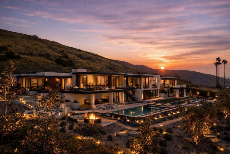 Modern hillside resort at sunset with lit villas, reflecting pool, and warm sky