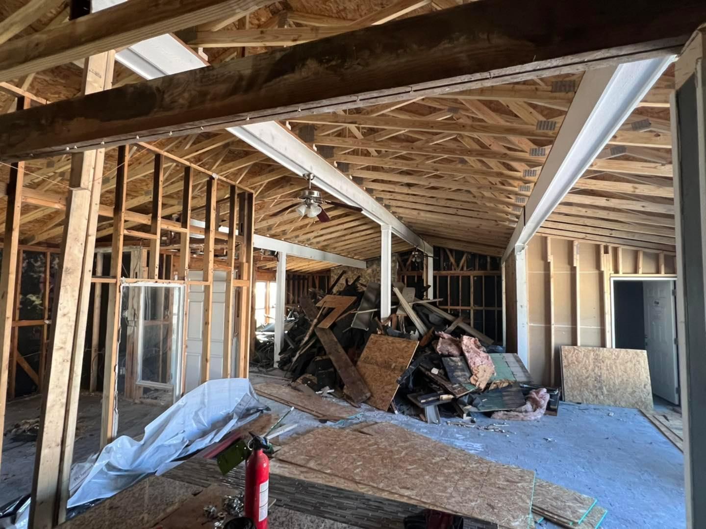 An interior view of a room under construction, showing exposed wooden ceiling rafters, wall framing, and a pile of debris.