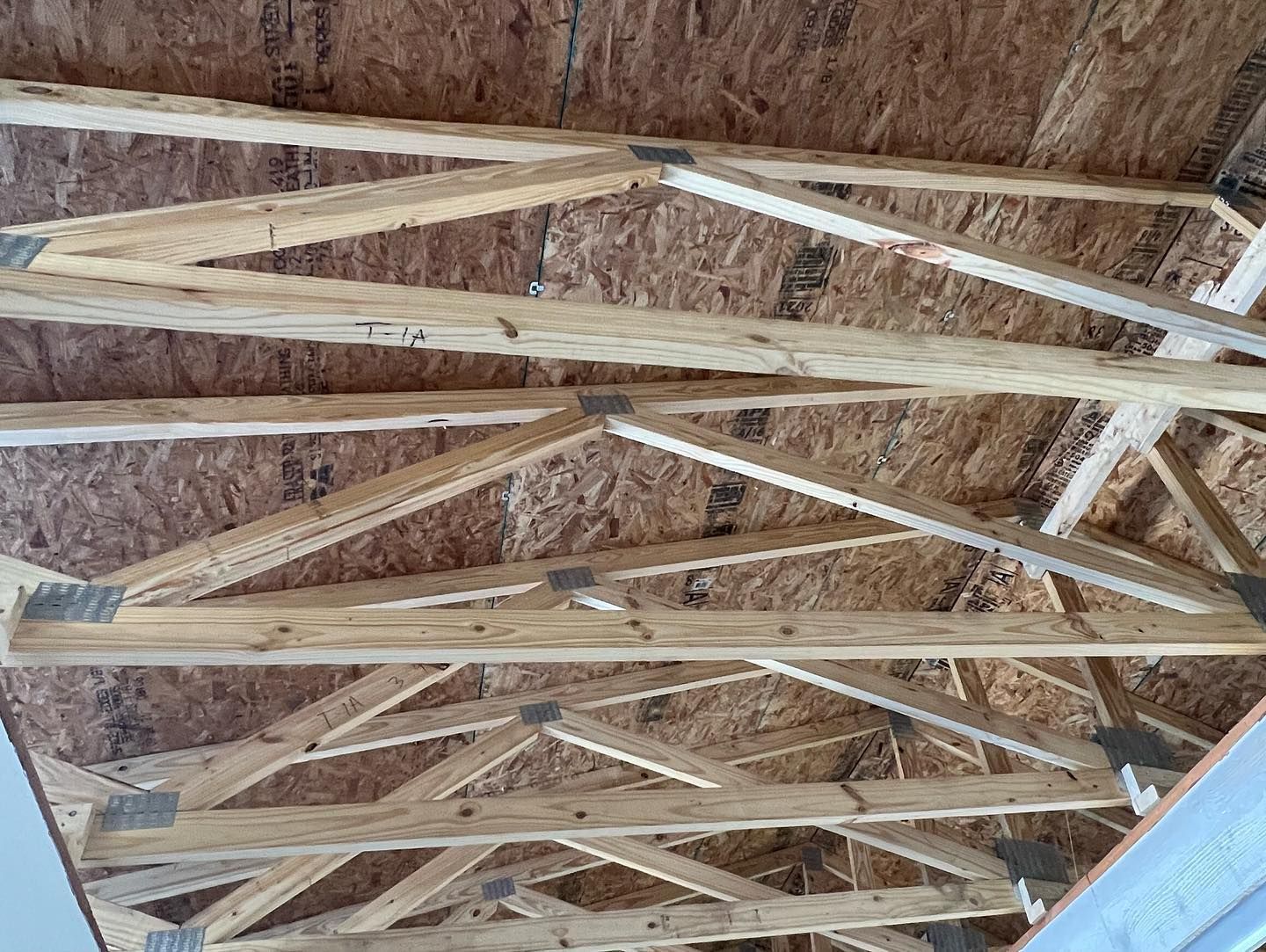Close-up view of wooden roof trusses supporting plywood sheathing inside an unfinished attic structure.