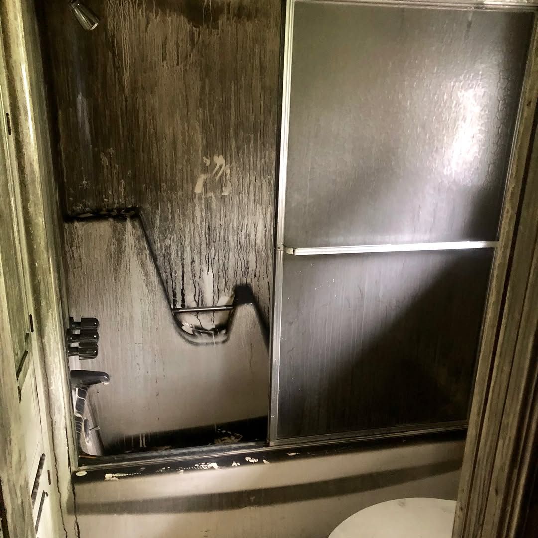 A shower stall featuring heavily stained, dark-streaked walls and glass sliding doors.