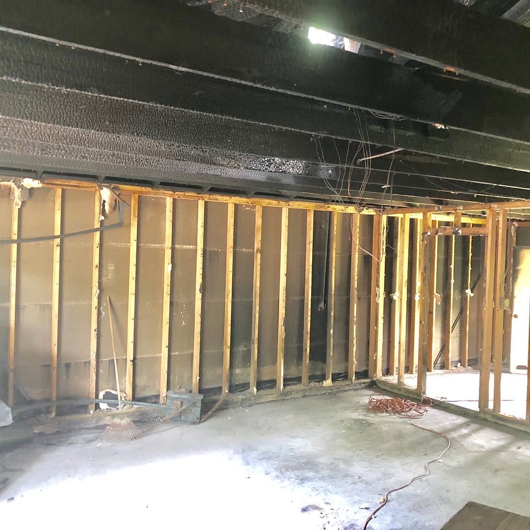 An unfinished room interior showing exposed wooden wall studs and charred black ceiling beams after a fire.