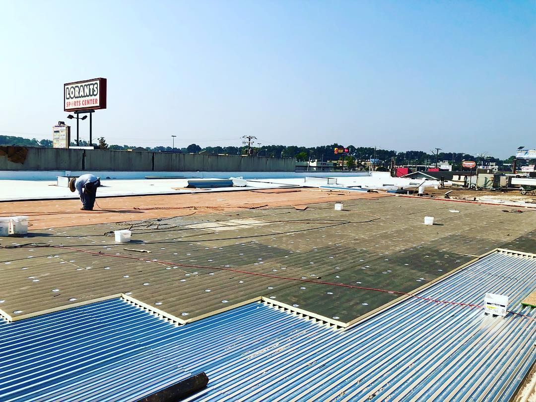 Construction workers installing a radiant heating pipe system on a flat rooftop with a billboard in the background.