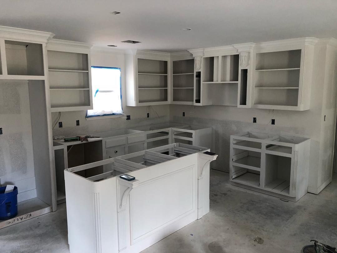 A kitchen in progress with freshly installed white cabinets, an island, and a window, during a home renovation.