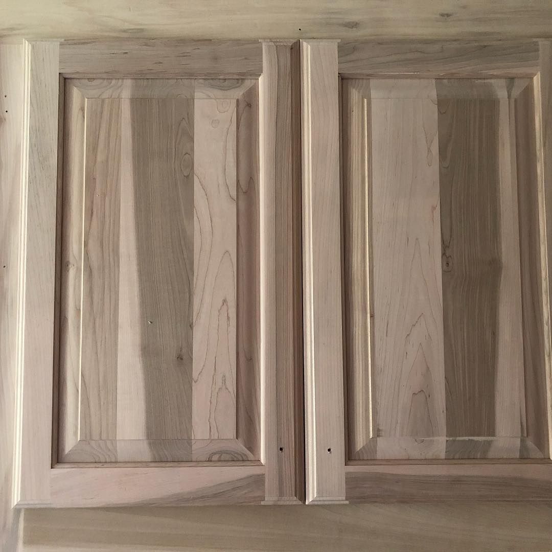 Two unfinished wooden cabinet doors with visible light and dark grain variations and beveled panel detailing.