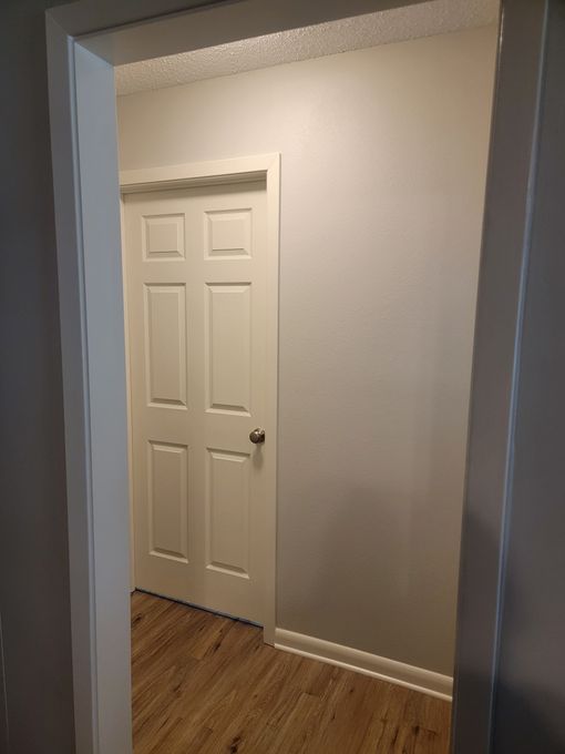 A view from a doorway looking into a room with light-colored walls, wood-look flooring, and a white six-panel door.