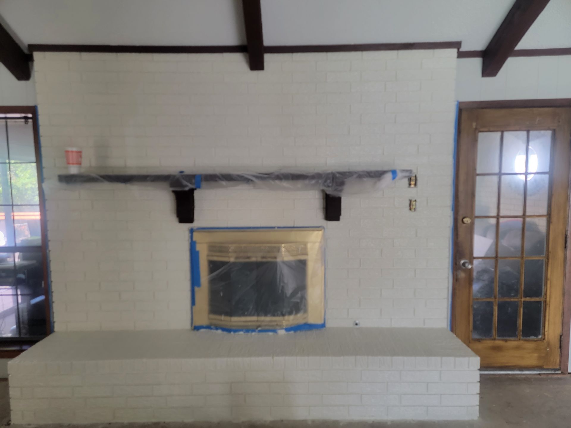A painted white brick fireplace and hearth under renovation, with the fireplace insert and mantle masked in plastic.