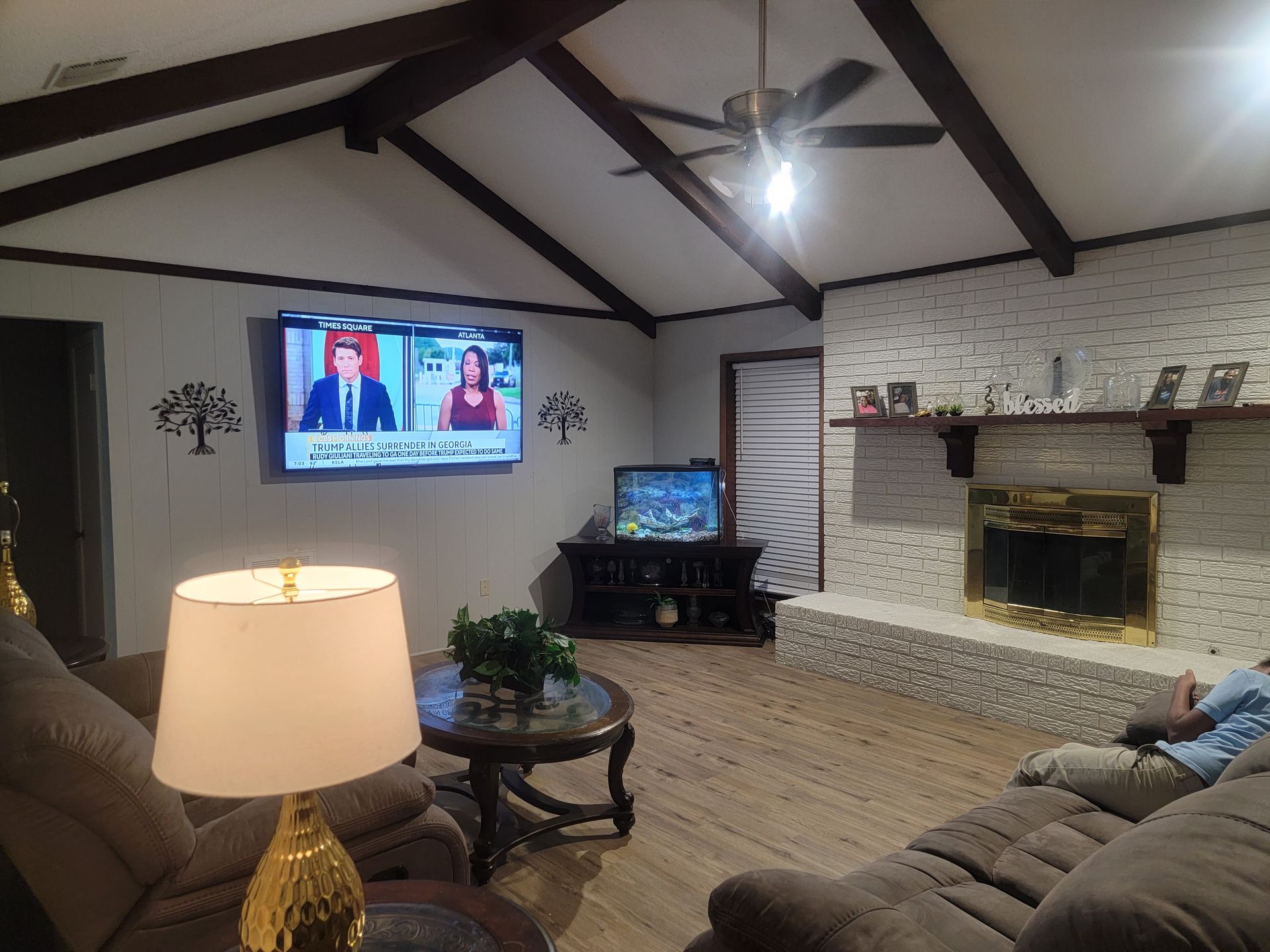 A living room with a stone fireplace, exposed ceiling beams, two televisions, and comfortable furniture.