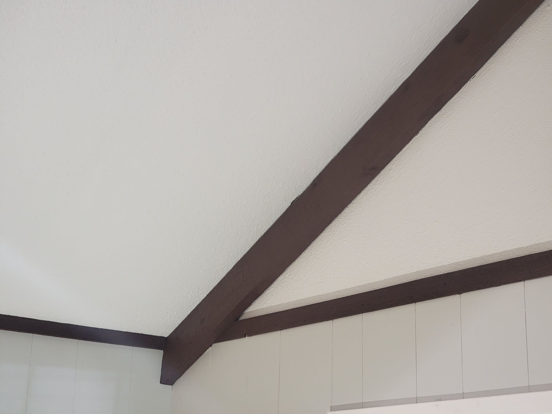 Dark brown wooden beams set against a white ceiling and walls in a minimalist interior space.