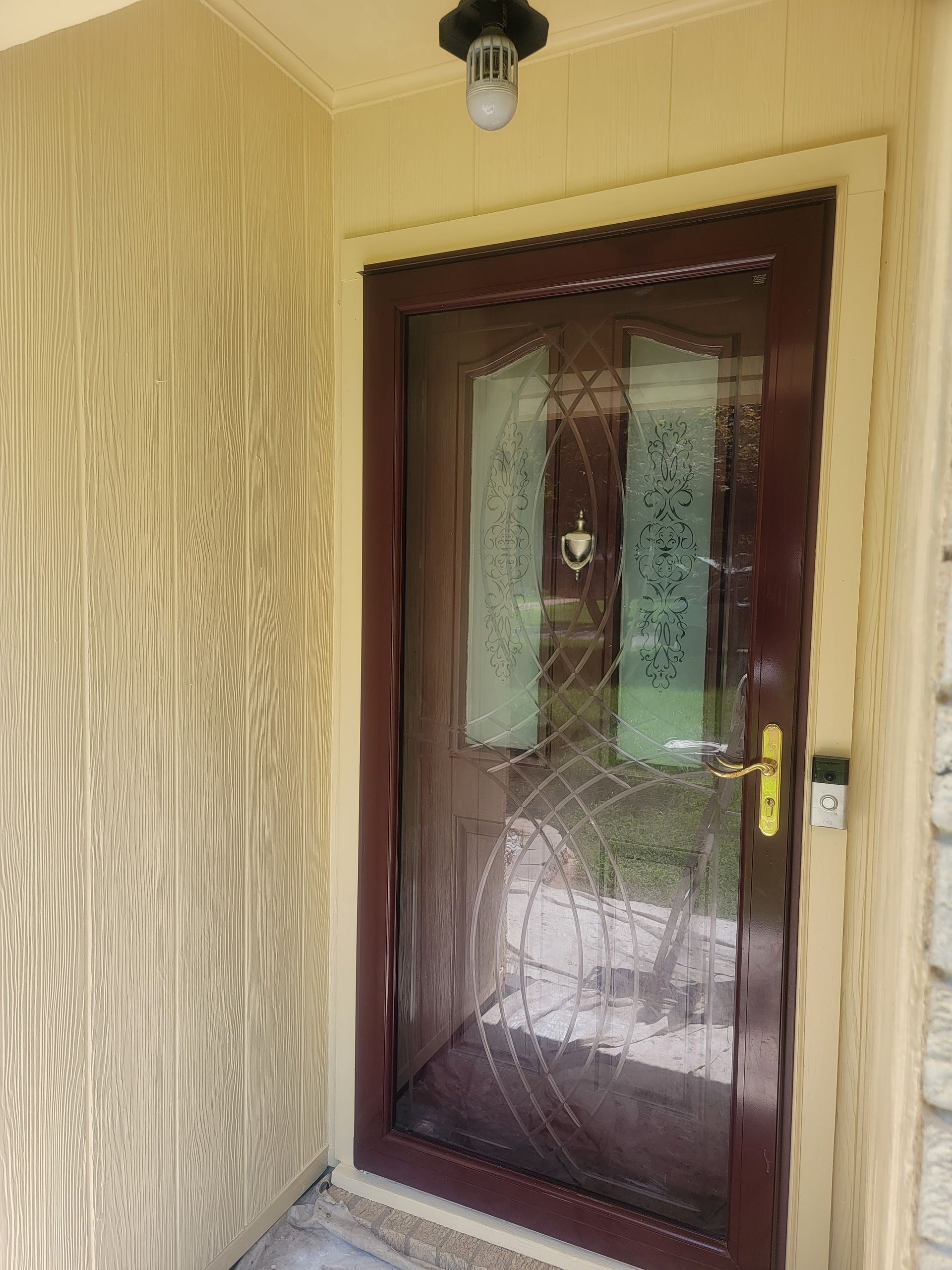 A front door with a dark brown storm door featuring decorative frosted glass panels, seen from a porch entryway.