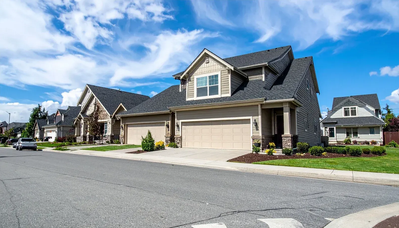 A residential house under construction, featuring wooden framing and OSB wall sheathing under a partly cloudy blue sky.