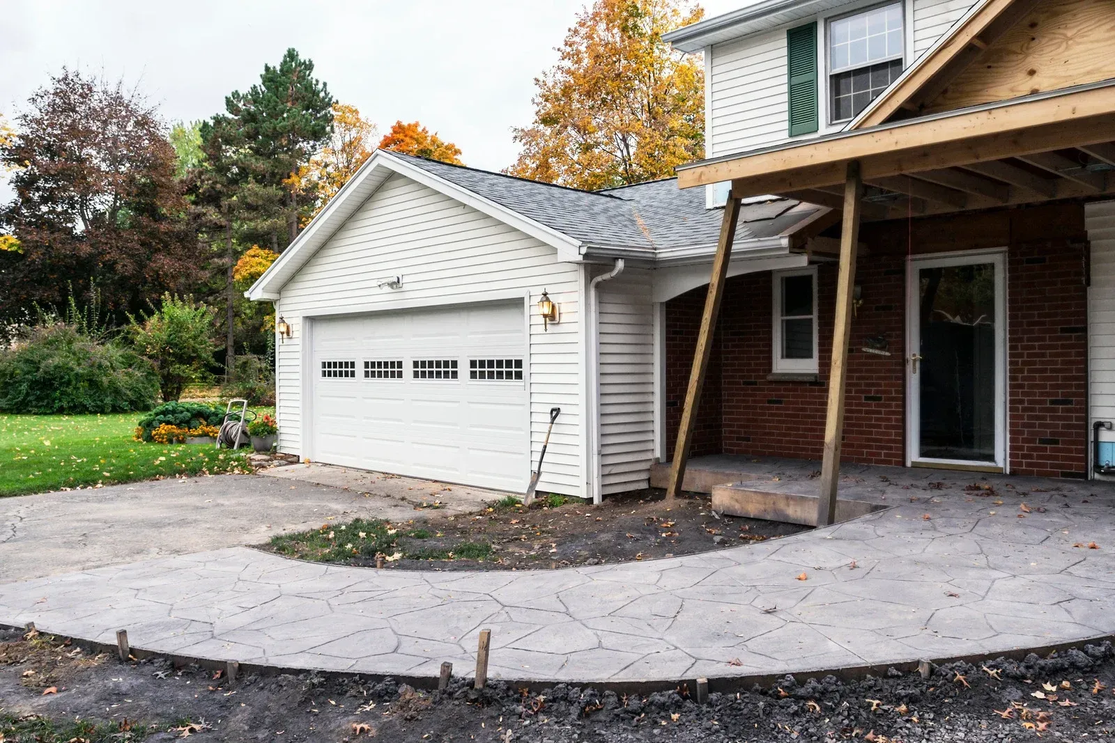 A white house with a garage and a large concrete patio under construction with wooden support beams in the yard.