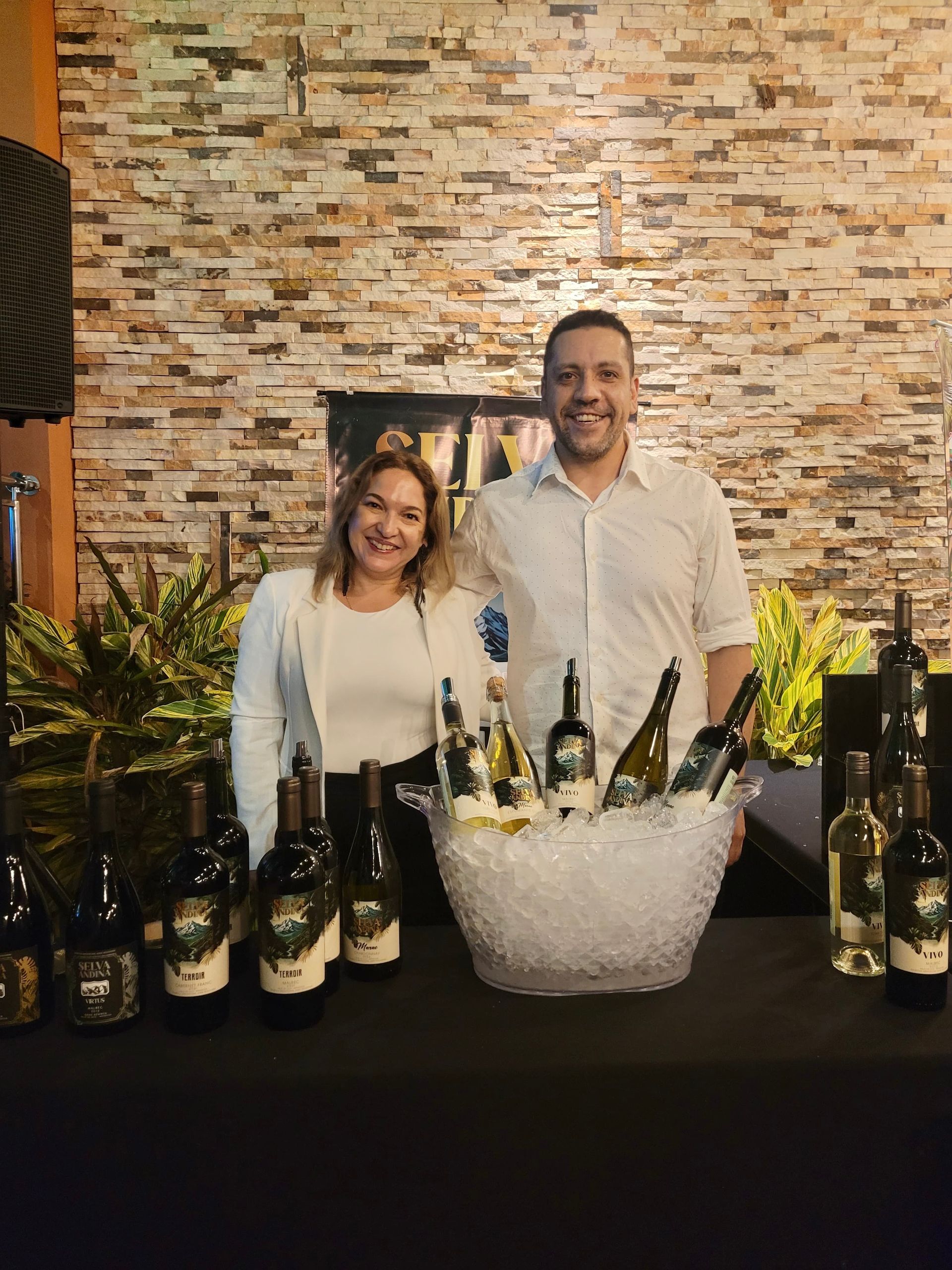 Dos personas en una cata de vinos, con botellas expuestas sobre una mesa negra; botellas sobre hielo.