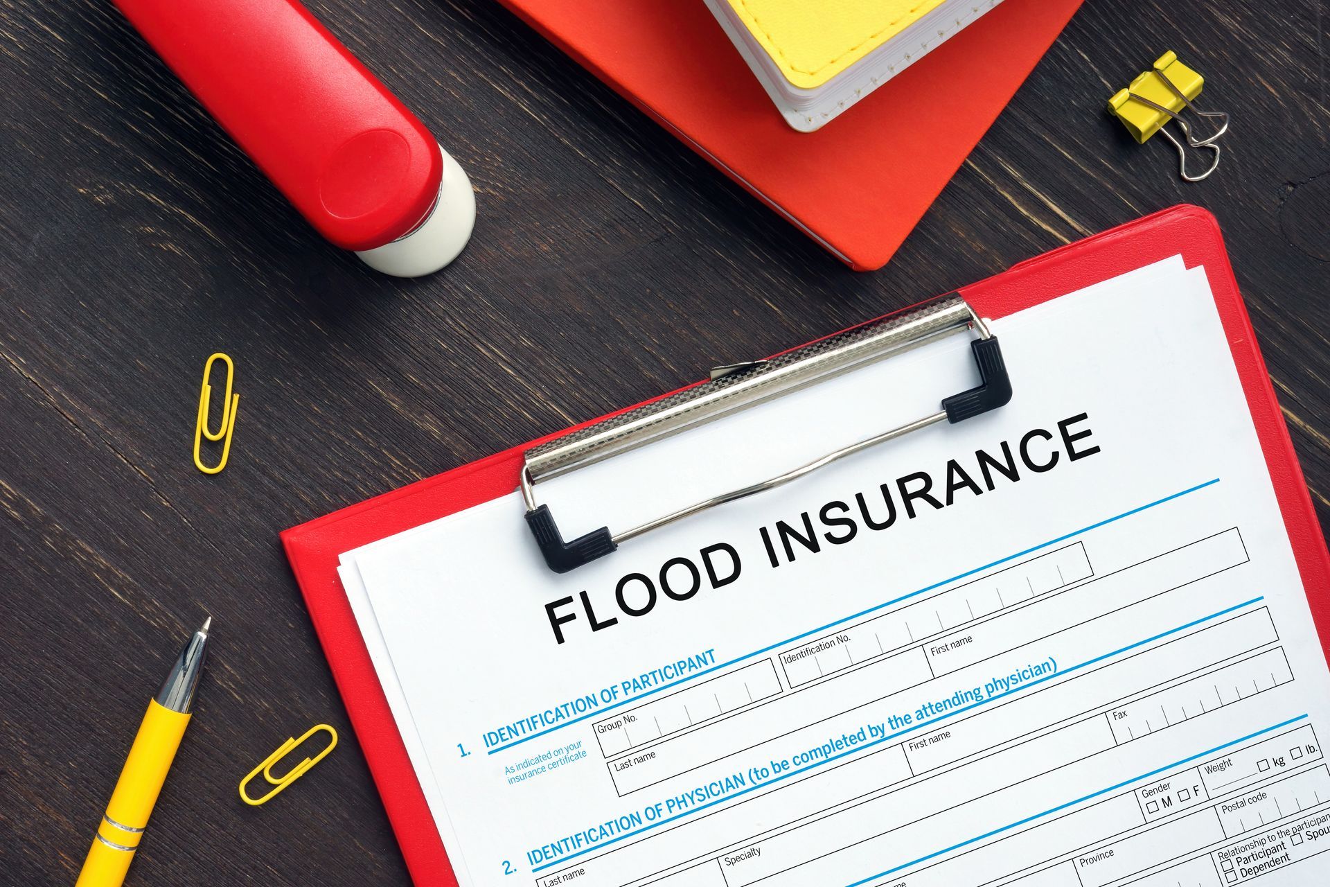 Flood insurance form on a clipboard with red office supplies on a dark desk