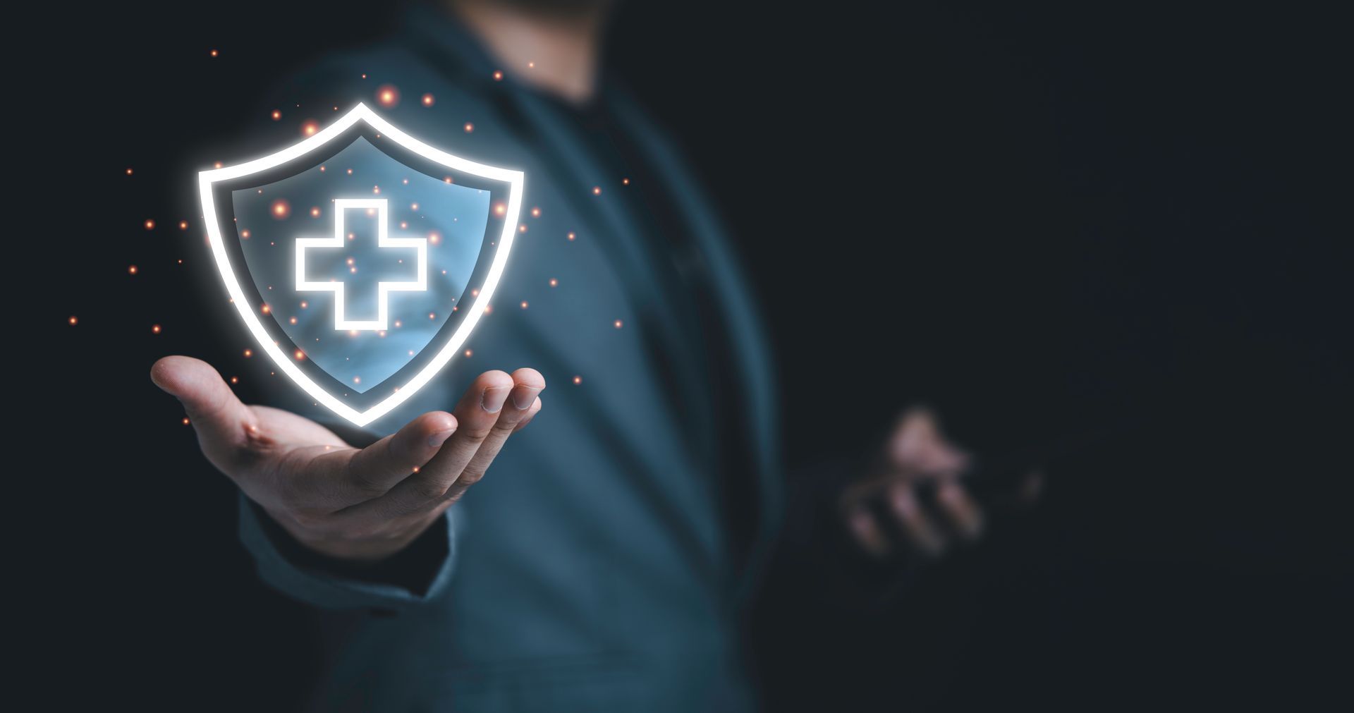 Hand holding glowing shield with medical cross icon on dark background