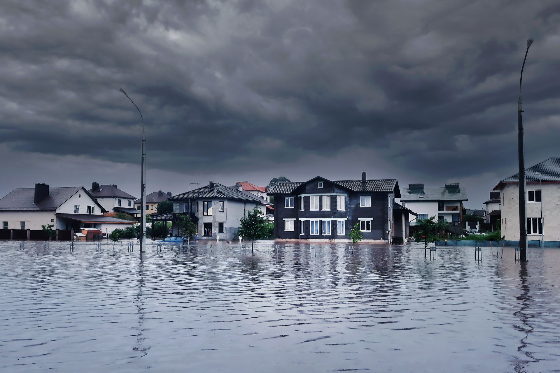 Flooded residential street with houses partially submerged under dark, stormy skies.
