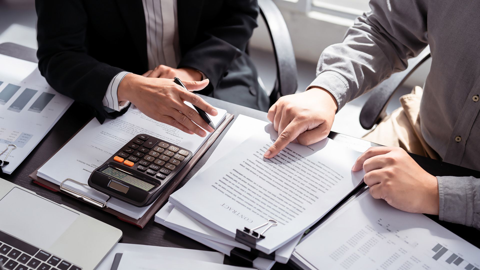 Two people review documents beside a calculator at a bright office desk.
