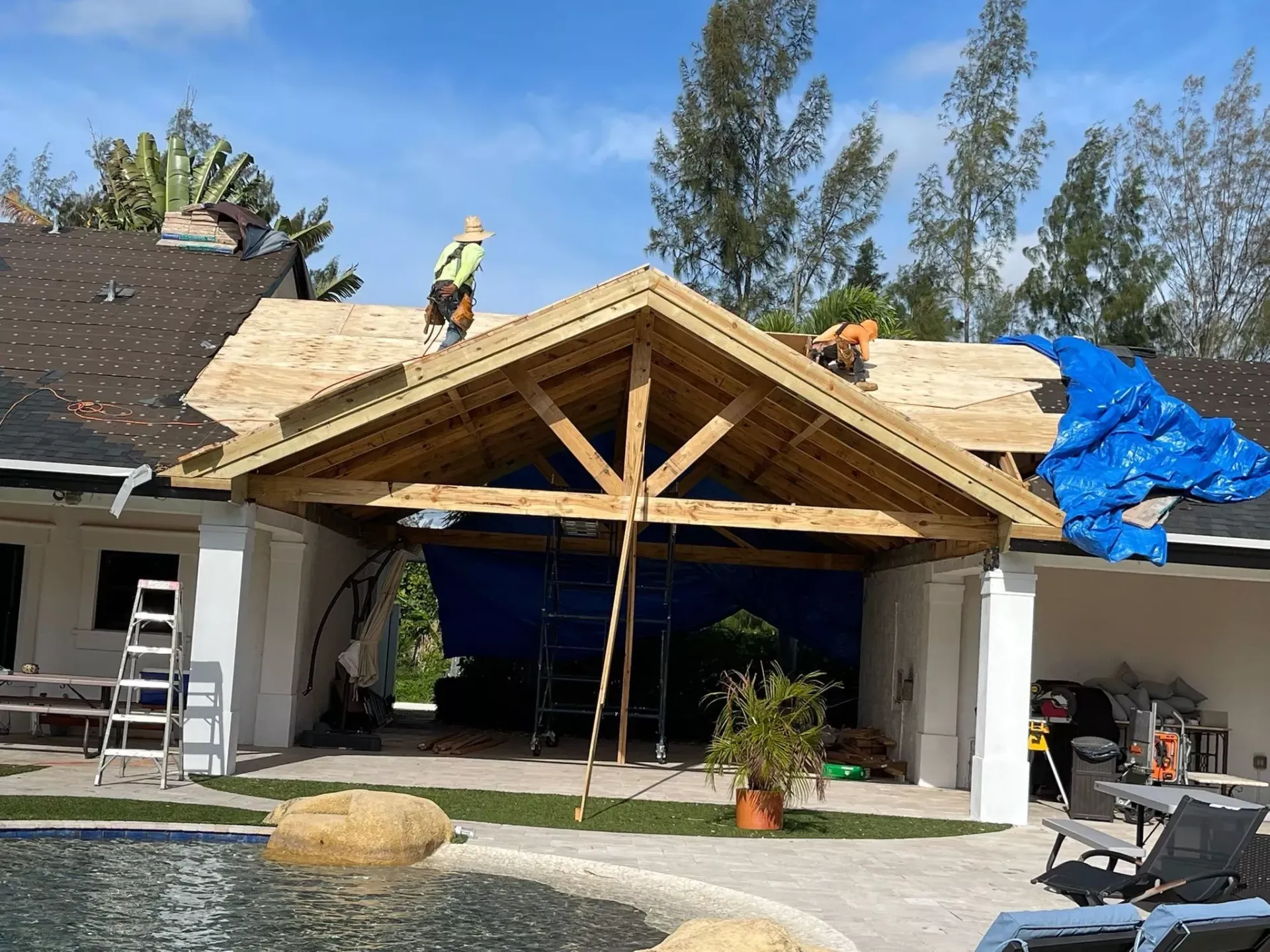 A man is working on the roof of a house next to a pool.
