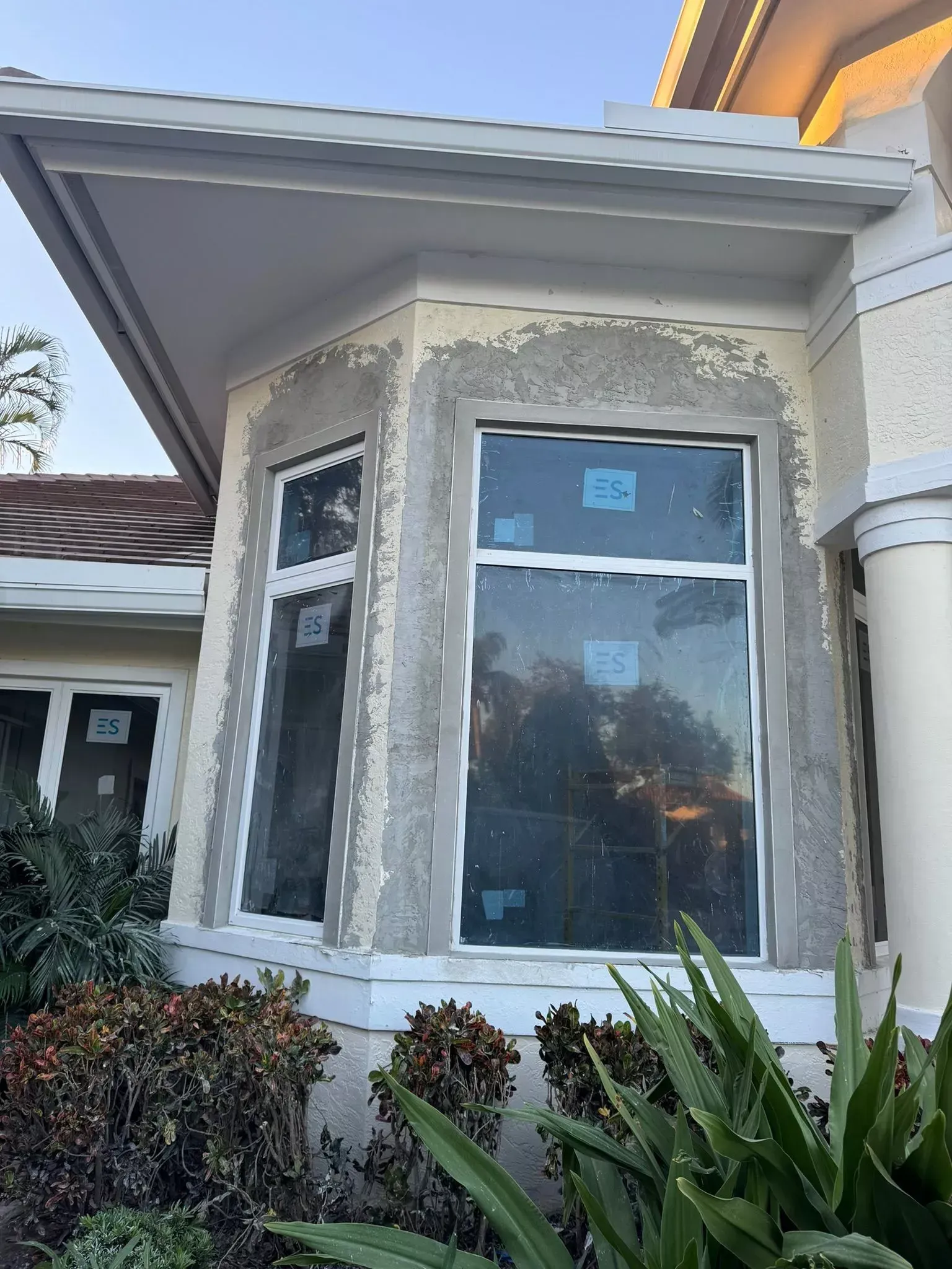 A large window on the side of a house with a lot of plants in front of it.