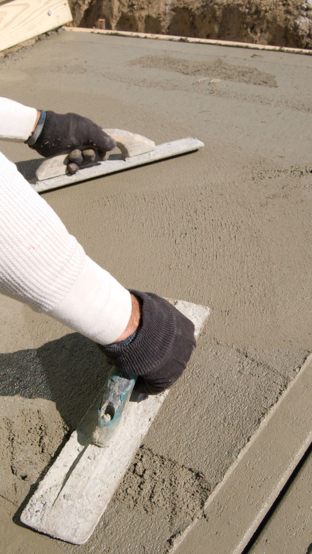A person is using a trowel to spread concrete on the ground.