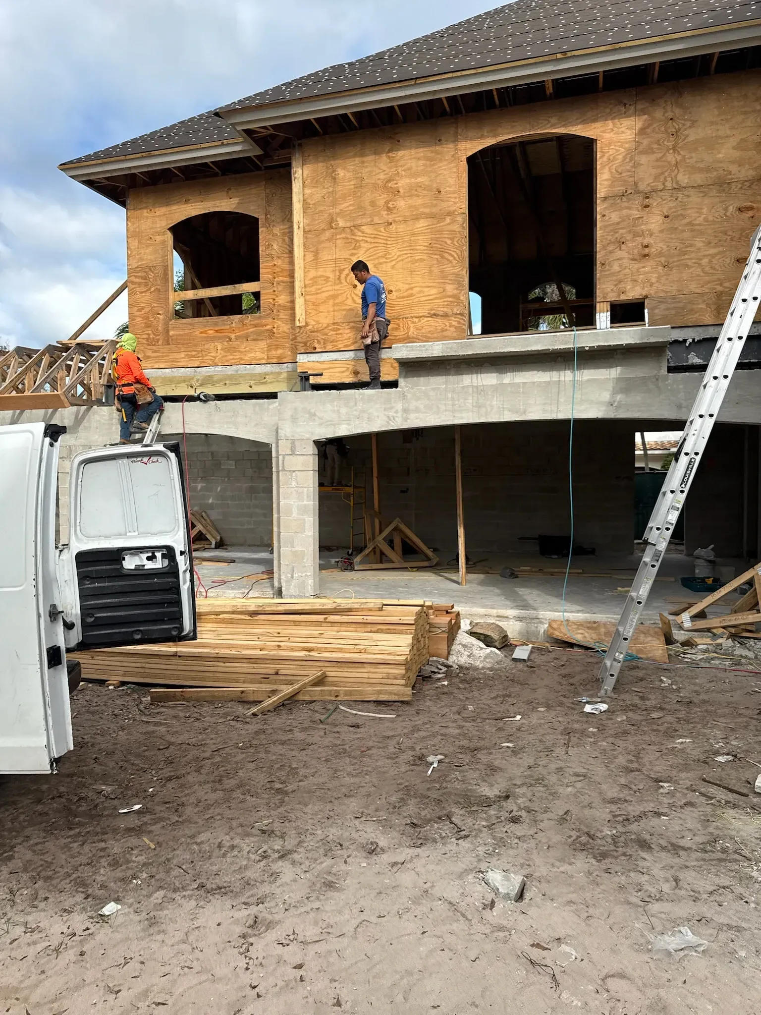 A white van is parked in front of a house under construction.
